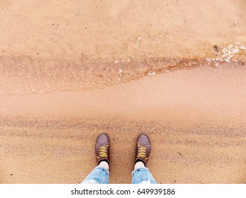 Looking down on a pair of brown leather shoes standing on a sandy ocean beach. Summer vacation concept. selective focus and toned image
