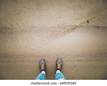 Looking down on a pair of brown leather shoes standing on a sandy ocean beach. Summer vacation concept. selective focus and toned image
