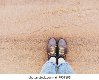 Looking down on a pair of brown leather shoes standing on a sandy ocean beach. Summer vacation concept. selective focus and toned image
