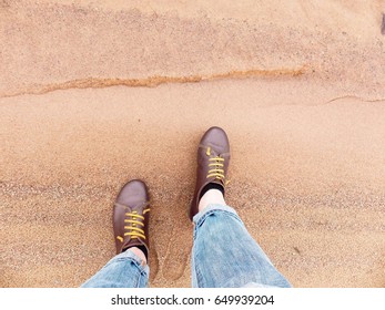 Looking down on a pair of brown leather shoes standing on a sandy ocean beach. Summer vacation concept. selective focus and toned image
