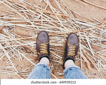 Looking down on a pair of brown leather shoes standing on a sandy ocean beach. Summer vacation concept. selective focus and toned image
