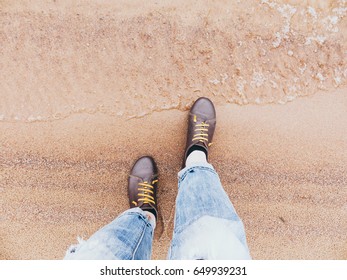 Looking down on a pair of brown leather shoes standing on a sandy ocean beach. Summer vacation concept. selective focus and toned image
