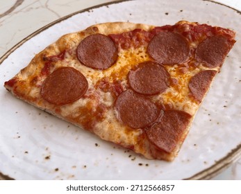Looking down on a slice of Pepperoni pizza on a white plate.