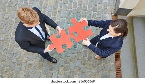 Looking Down On Two Business People Solving A Big Red Jigsaw Puzzle