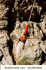 Looking Down Onto Unidentifiable Young Man Suspended From Bungee Jump Cord Over Rock Canyon Walls 