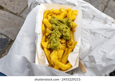 Looking down at an open portion of chips and mushy peas being eaten outside