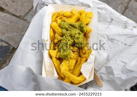 Looking down at an open portion of chips and mushy peas being eaten outside