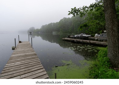 Looking down a pier on a calm Wisconsin lake on a foggy morning.  Fishing boat in distance. - Powered by Shutterstock
