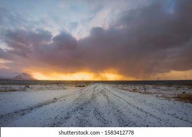 Looking down a road in Iceland, with a sunset sky on fire and storm clouds