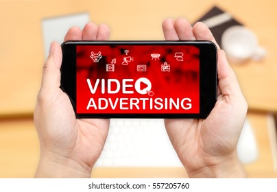 Looking Down To See Two Hand Holding Mobile Phone With Video Advertising Word On Screen And Blur Desk Office Background,Digital Content Concept