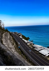 Looking down from a steep cliff to a beautiful coastal highway next to the deep blue ocean with local stalls lined along the seaside.