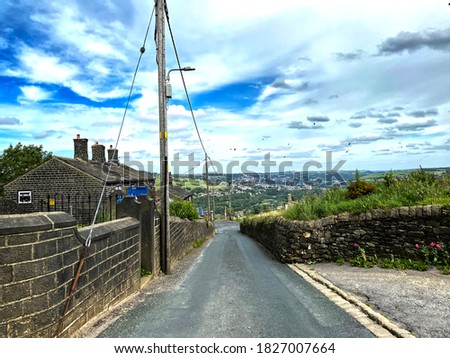 Looking down, Steep Lane, with a long stone wall, with houses in the distance in, Sowerby Bridge, Halifax, UK