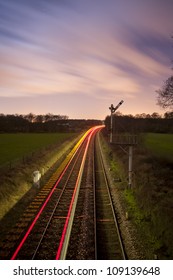 looking down a train line off a bridge with an oncoming train leaving light trails at night