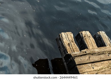 looking down at a weathered wood structure next to calm, reflective water with ripples and reflections and space for copy. vacation vibes design element or abstract background