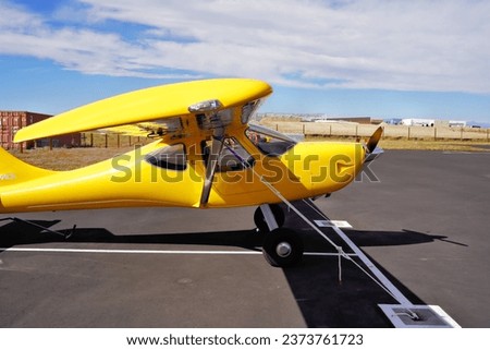 Looking Down the Wing of a Small Yellow Airplane Tied Down at an Airport