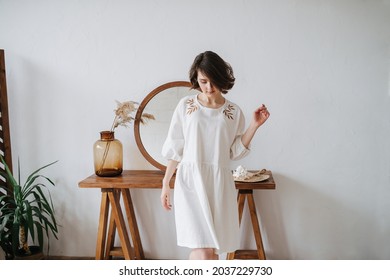 Looking down young woman in summer dress inside a room. Pretty brunette with short hair indoors. Mirror in background. Longshot.