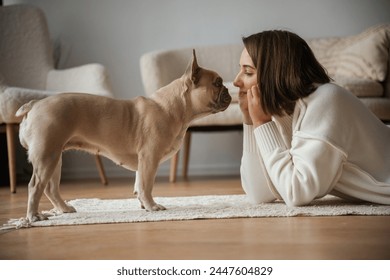Looking at each other, lying down on floor. Young woman is with her pug dog at home.