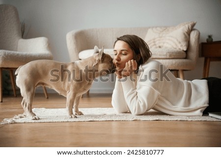 Looking at each other, lying down on floor. Young woman is with her pug dog at home.