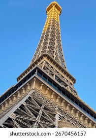 Looking up at the Eiffel Tower replica in Las Vegas against a bright blue sky, capturing the iconic architecture and tourist attraction in a clear sunny day setting.