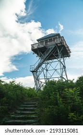 Looking up at a fire lookout tower in North Carolina on a sunny summer afternoon with a few clouds in the sky.