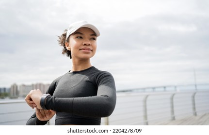 Looking at the fitness watch, the woman smiles and trains fitness in a tight-fitting tracksuit and cap. - Powered by Shutterstock