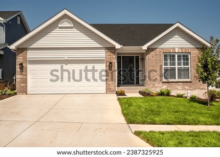 Looking at the front of a new one story brick ranch home with a gable roof in residential neighborhood subdivision with garage and double concrete driveway.