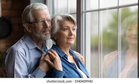 Looking in future. Loving senior man husband embrace aged wife from behind support encourage share feeling of beloved woman. Elderly spouses hug look at window meet twilight years together. Copy space - Powered by Shutterstock