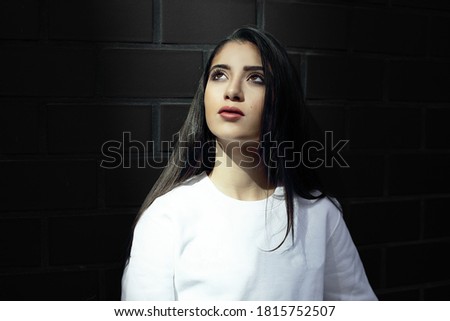 up looking girl standing in front of dark black brick wall having a moment, belive in hope and a better future while her eyes spot a light ray