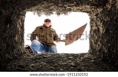 Looking up from a grave. A man stands with a shovel at the edge of the grave.