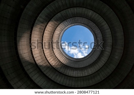Looking up from inside an industrial cooling tower. With blue sky and white clouds above the chimney