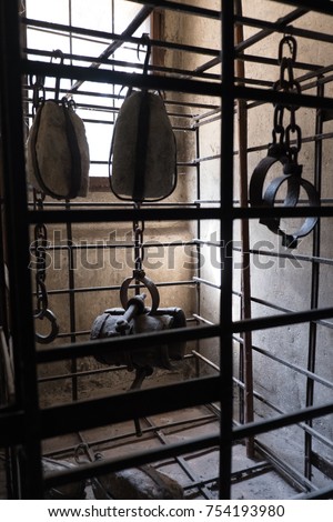 Looking inside a prison cell in an old castle in Europe with various devices of torture. Manacles and torture devices hanging from chains in a jail cell in a medieval castle.