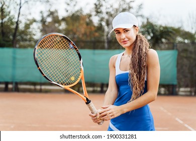 Looking into the camera. Beautiful, young, european woman confidently hits the ball on the tennis court during training. Determined to win. Dressed in stylish sports tennis uniform - dress.