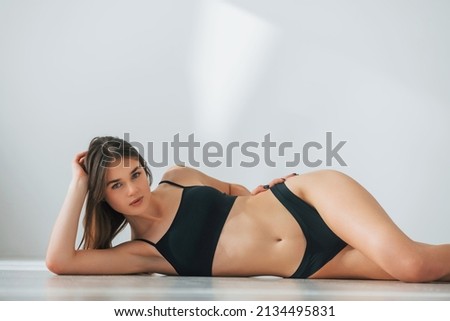 Looking into camera. Laying down on the floor. Beautiful woman in underwear is posing indoors.