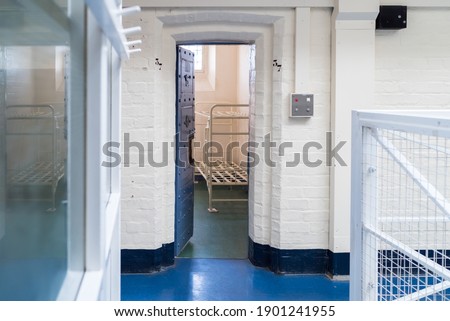 Looking into prison cell block victorian British English jail house with bed in room lock up high security room derelict old new category A B C in custody with bars door open confined escaping