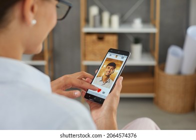 Looking for love online: Single woman hits red heart icon on smartphone display and gives like to happy handsome young man on mobile dating app or marriage Internet website. Closeup view over shoulder - Shutterstock ID 2064574376
