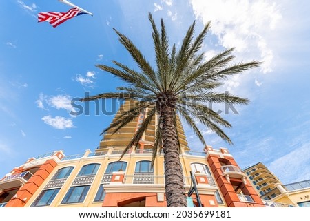 Looking up low angle view on shopping mall with American flag and store buildings architecture by Destin Harborwalk Village, Florida Panhandle with palm tree, blue sky