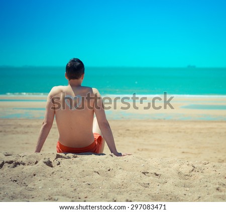 looking at a man his back on the beach he is looking and relaxing at the seaside in retro old fashioned style. There is a heart painted on him with suncream