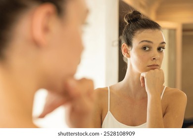 Looking in mirror, young woman contemplating with hand on chin at home. Reflection, self-examination, contemplation, thinking, introspection, self-care - Powered by Shutterstock