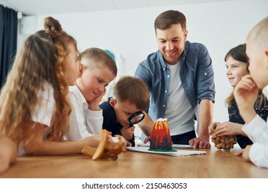 Looking At The Model Of Volcano. Group Of Children Students In Class At School With Teacher.