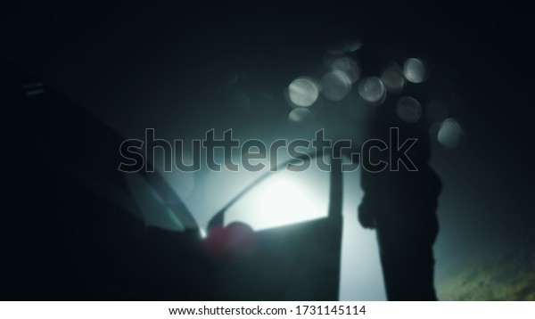Looking up at a mysterious figure, standing next to\
a car with the door open, underneath a street light at night. With\
a blurred, bokeh edit