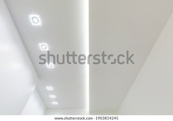 looking up on suspended ceiling\
with halogen spots lamps and drywall construction in empty room in\
apartment or house. Stretch ceiling white and complex\
shape.