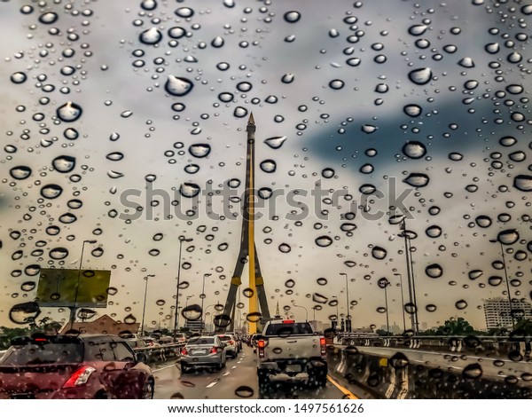 Looking out from car, raining outside, blur\
photo, focus water dropping. View of traffic jam on the bridge over\
the river, Bangkok,\
Thailand.