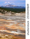 looking out over colorful hot  springs and microbial mats towards the gallatin mountains in the porcelain  basin of norris geyser basin on  sunny summer day in yellowstone national park, wyoming      