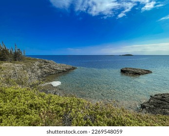 Looking out over the vast expanse and pure waters of Lake Superior from the rocky coast. A stone basin is in the forefront of view.  Small islands covered in green evergreen trees in the distance. - Powered by Shutterstock