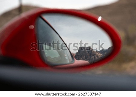Looking out the side view mirror of a red sports car.  A mountain of Nevada in the backdrop.