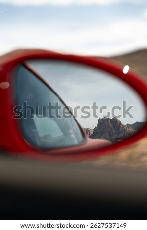 Looking out the side view mirror of a red sports car.  A mountain of Nevada in the backdrop.