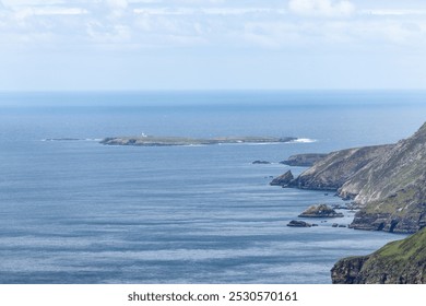 Looking out towards the Slieve League cliffs, a solitary island with a lighthouse stands in the Atlantic Ocean. The blue hues of the ocean and sky blend together - Powered by Shutterstock