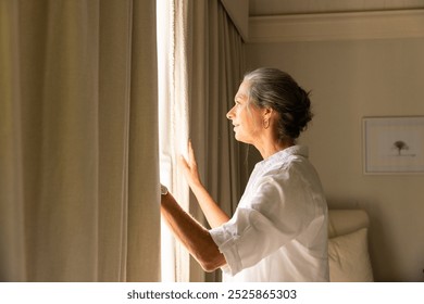 Looking out window, mature woman in white shirt enjoying peaceful moment at home, copy space. Relaxation, reflection, tranquility, serenity, contemplation, indoors - Powered by Shutterstock