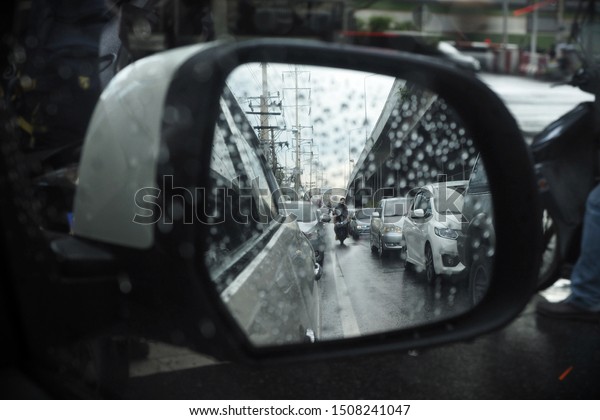 Looking\
outside the car window in the raining day. Traffic jam on the road\
side view. People ride motorcycle in side\
mirror.