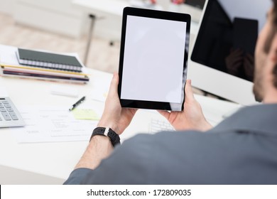 Looking Over The Shoulder Of A Young Businessman Sitting At His Desk Using A Tablet Computer With The Blank White Screen Viewable